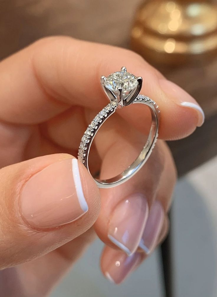 Silver ring with a diamond held by a hand with light pink nail polish